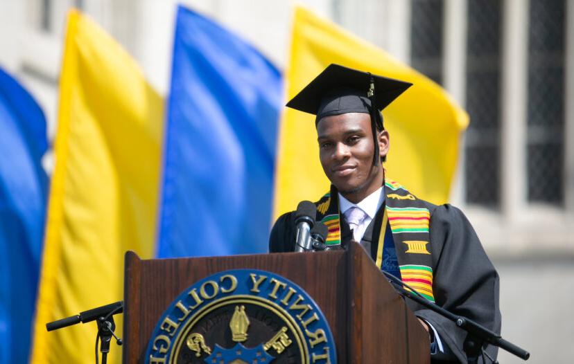 A trinity college grad standing at the graduation podium ready to speak